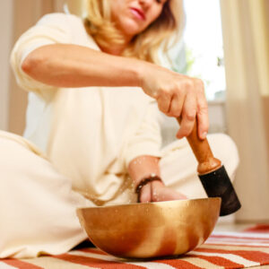 Woman playing on a tibetian singing bowl in cozy room meditating in a yoga
